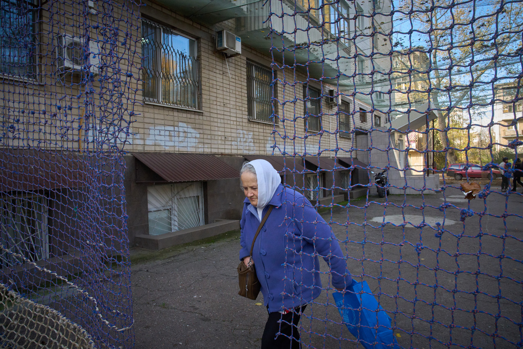 A local resident walks in a yard covered with an anti-FPV-drone net in the frontline city of Kherson, Southern Ukraine, Monday, Nov. 3, 2025. (AP Photo/Efrem Lukatsky)