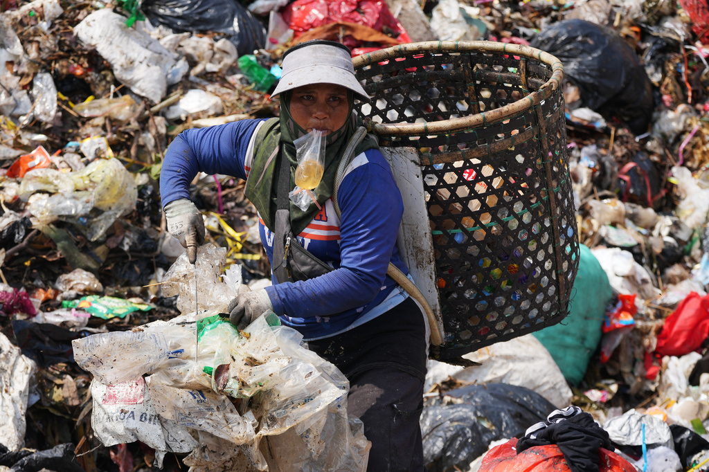 A waste picker drinks water from a plastic bag as she looks for recyclable items in a pile of garbage at the Bantargebang landfill on the outskirts of Jakarta, Indonesia, Monday, July 6, 2026. (AP Photo/Tatan Syuflana)