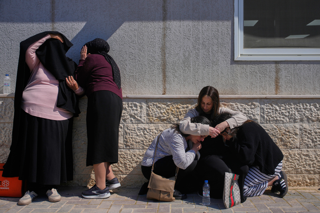 Mourners take cover while air-raid sirens warn of incoming missiles launched by Iran toward Israel during the funeral of Sarah Elimelech and her daughter Ronit who were killed in an Iranian missile attack, in Beit Shemesh, Israel, Monday, March 2, 2026. (AP Photo/Ohad Zwigenberg)