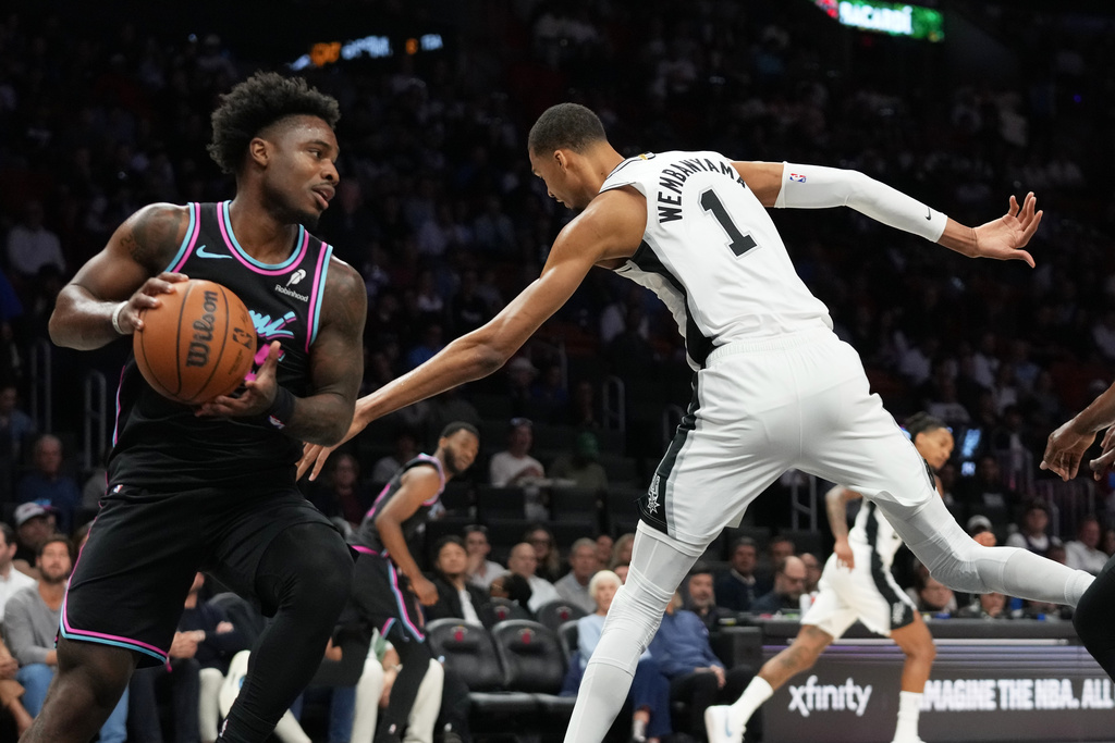 Miami Heat's Davion Mitchell, left, grabs a rebound over San Antonio Spurs forward Victor Wembanyama (1) during the first half of an NBA basketball game, Monday, March 23, 2026, in Miami. (AP Photo/Lynne Sladky)