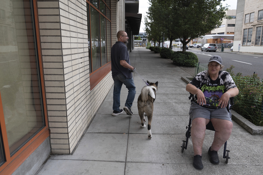 With the U.S. Immigration and Customs Enforcement building at background right, Rick Stype walks his dog past his neighbor, Cindy Colgrove, outside the apartment complex where they live in Portland, Ore., on Tuesday, Sept. 9, 2025. (AP Photo/Jenny Kane)