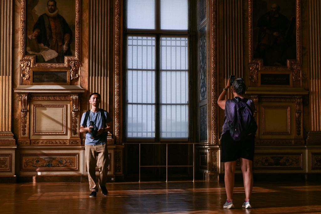 Visitors take a picture of the window which was broken during the reopening to the public of the Apollo Gallery, at the Louvre museum in Paris, Wednesday, July 22, 2026. (Lou Benoist/Pool Photo via AP)