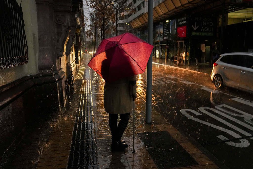 A woman waits for a bus during a rainstorm in Santiago, Chile, early Monday, July 20, 2026. (AP Photo/Esteban Felix)