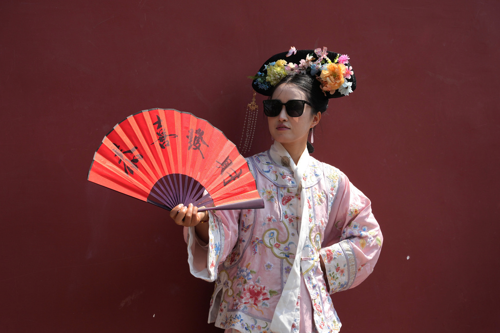 A woman holds up a fan with the words "May you be happy and prosperous" wearing historical Chinese costume outside the Forbidden City in Beijing on Saturday, April 4, 2026. (AP Photo/Ng Han Guan)