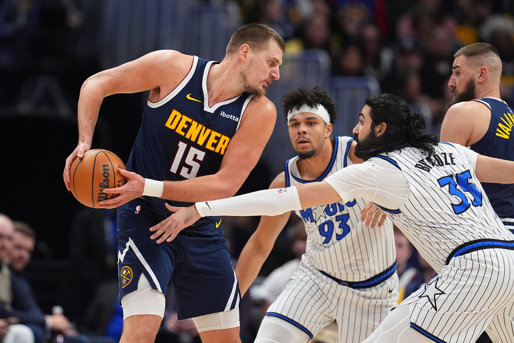 Denver Nuggets center Nikola Jokić, left, looks to pass the ball as Orlando Magic center Goga Bitadze, front right, and guard Noah Penda defend in the first half of an NBA basketball game, Thursday, Dec. 18, 2025, in Denver. (AP Photo/David Zalubowski)