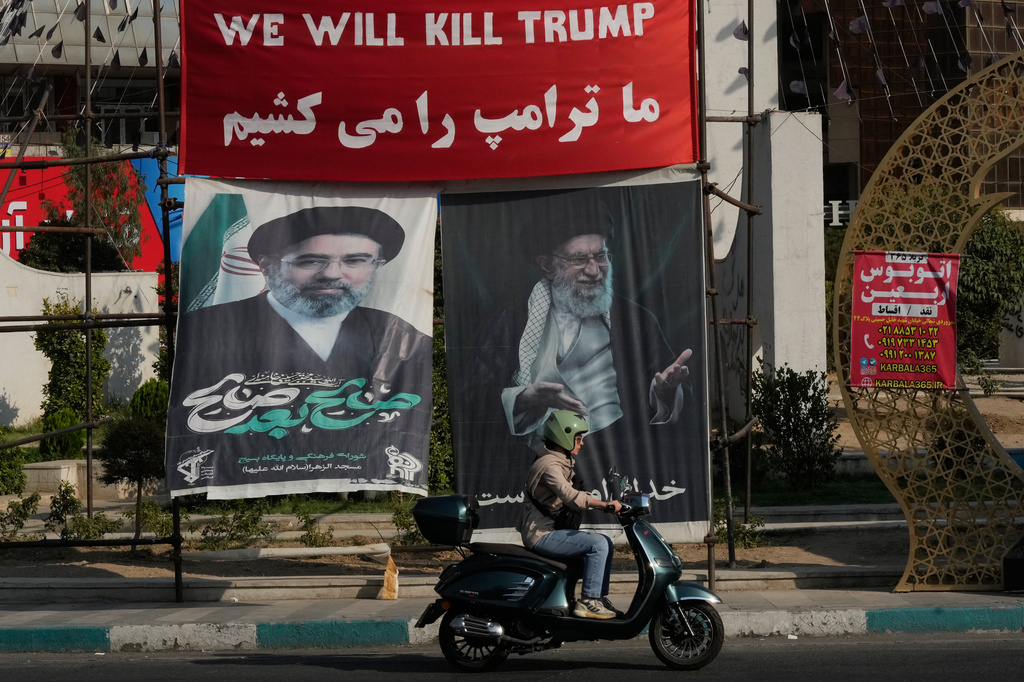 A motorbike drives past a banner reading in English and Farsi, "We will kill Trump," and banners showing portraits of the late Iranian Supreme Leader Ayatollah Ali Khamenei, right, and his son Ayatollah Mojtaba Khamenei, the successor to him, at a square in Tehran, Iran, Monday, Aug. 10, 2026. (AP Photo/Vahid Salemi)