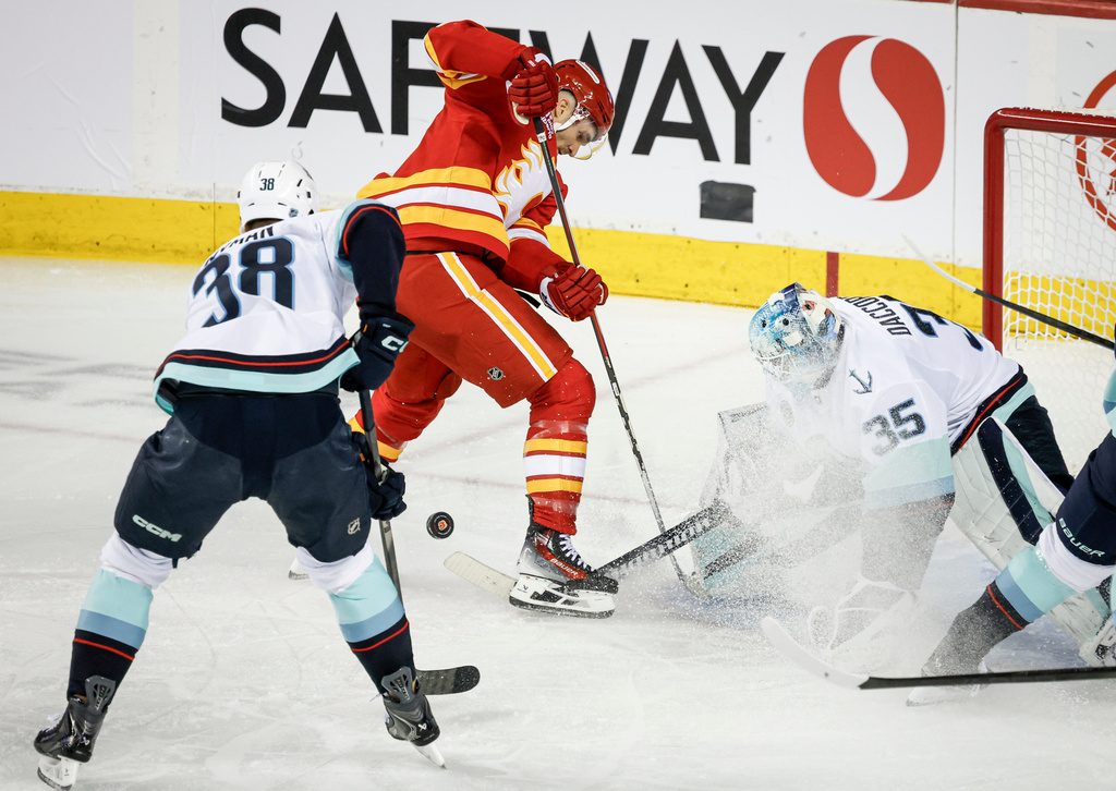 Seattle Kraken goalie Joey Daccord (35) hits the puck away from Calgary Flames' Jonathan Huberdeau, center top, during second-period NHL hockey game action in Calgary, Alberta, Thursday, Dec. 18, 2025. (Jeff McIntosh/The Canadian Press via AP)