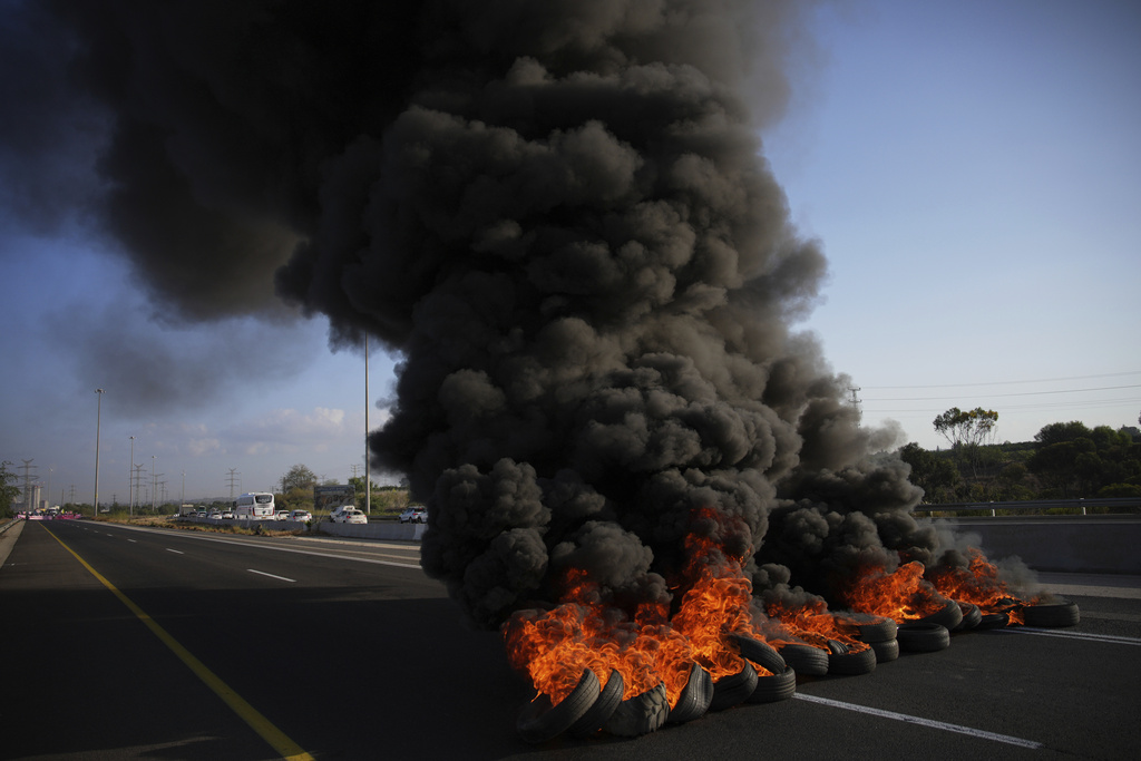 Tires are set on fire to block a road during a protest demanding the immediate release of hostages held by Hamas and calling for the Israeli government to reverse its decision to take over Gaza City and other areas in the Gaza Strip, near Jerusalem, Israel, Sunday, Aug. 17, 2025. (AP Photo/Ohad Zwigenberg)