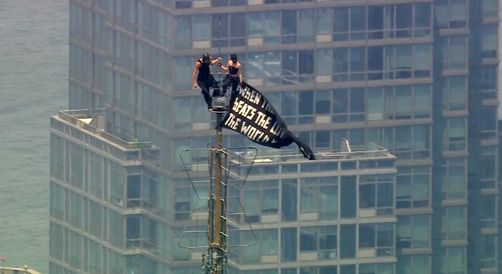 Two people stand on the tip of the antenna of the Empire State Building in New York while holding a banner on Wednesday, July 1, 2026. (WABC-TV via AP)