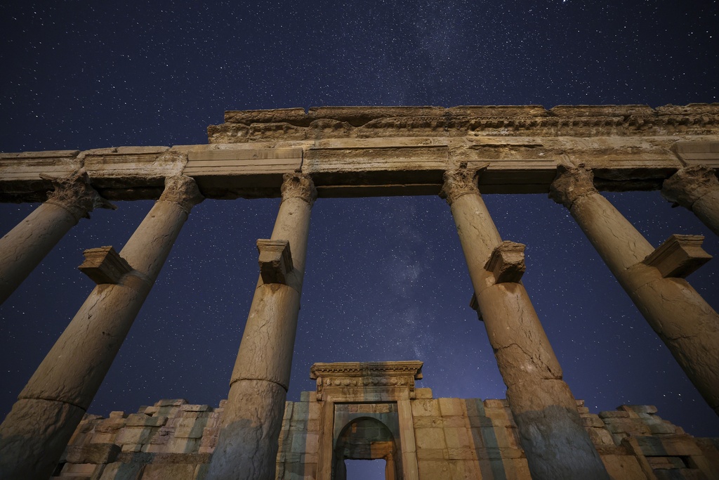Columns of the Long Street, foreground, and the rear gate of the Roman Theater in the ruins of the ancient city of Palmyra are seen under a star-studded sky in Syria, late Wednesday, Aug. 27, 2025. (AP Photo/Ghaith Alsayed)