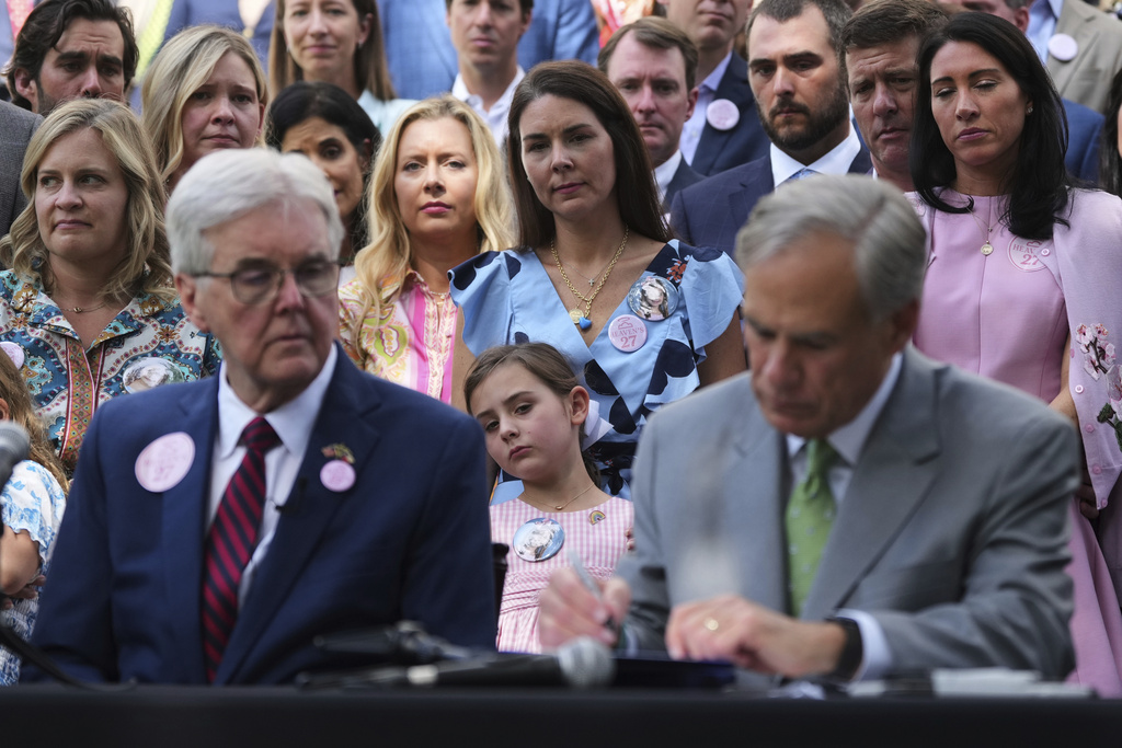 ADDS NAMES: Emmalynn Lytal, center, sister of Kellyane Lytal, stands with her mother Malorie Lytal, and other family of children who died at Camp Mystic as they watch Texas Gov. Greg Abbott, right, sign camp safety bills into law, Friday, Sept. 5, 2025, in Austin, Texas. (AP Photo/Eric Gay)