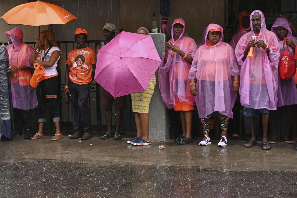 Supporters of the People's National Party wait in line in the rain outside a polling station to vote during general elections in Kingston, Jamaica, Wednesday, Sept. 3, 2025. (AP Photo/Collin Reid)