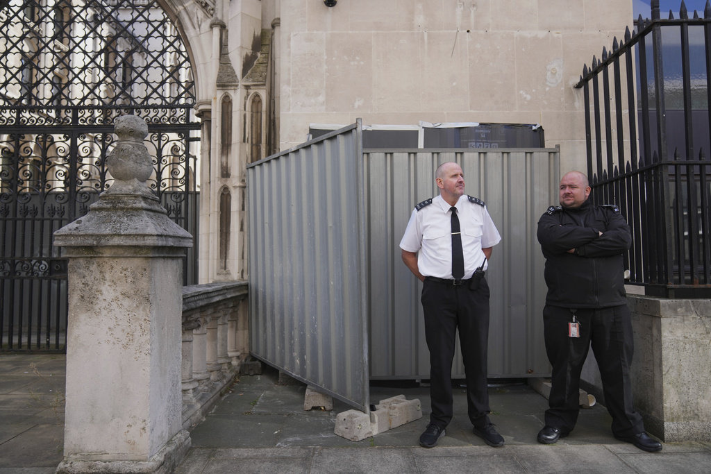 Security officials stand in front of large sheets of black plastic and two metal barriers which conceal street artist Banksy's latest artwork, a protester lying on the ground holding a blood-splattered placard while a judge in a traditional wig and black gown beats him with a gavel, outside at the Royal Courts of Justice in London, Monday, Sept. 8, 2025. (AP Photo/Joanna Chan)