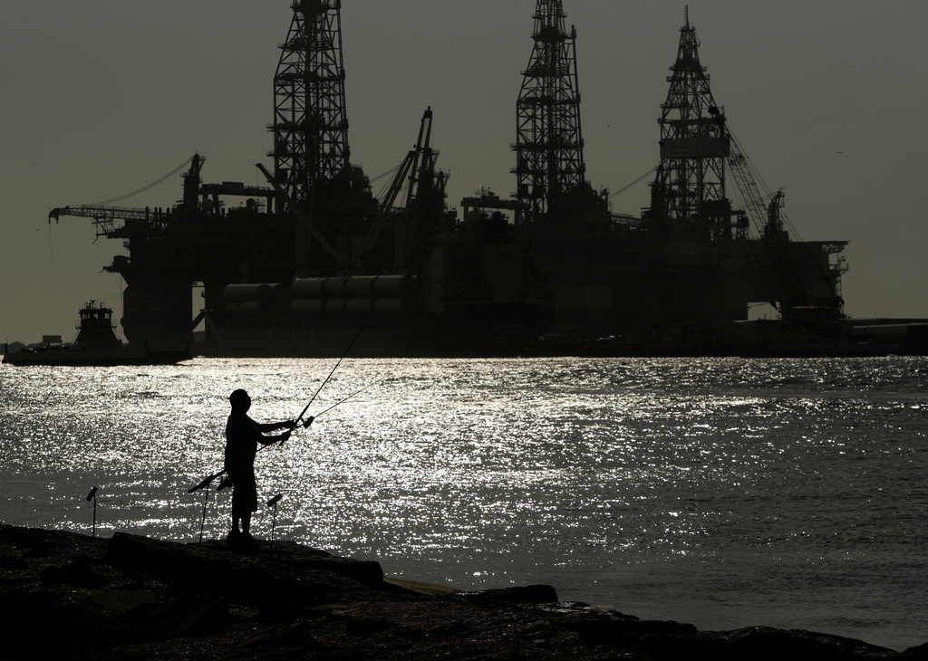 FILE - A man fishes near docked oil drilling platforms May 8, 2020, in Port Aransas, Texas. (AP Photo/Eric Gay, File)