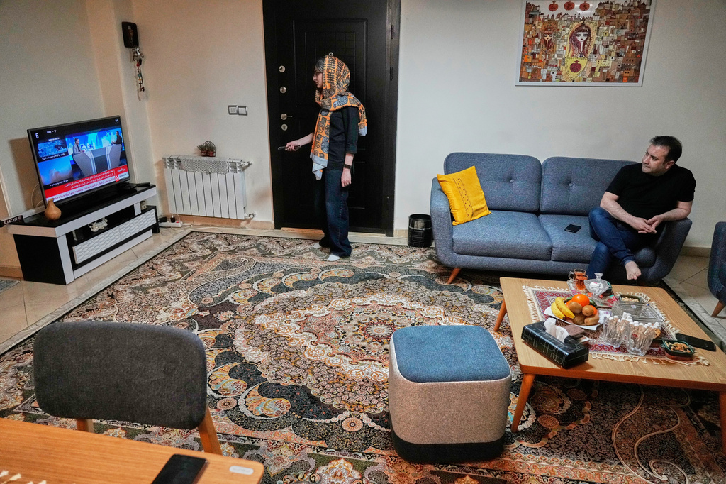 Zahra Arghavan, center, and Mehdi Alishir watch the news on TV in their living room in Tehran, Iran, Sunday, April 5, 2026. (AP Photo/Vahid Salemi)