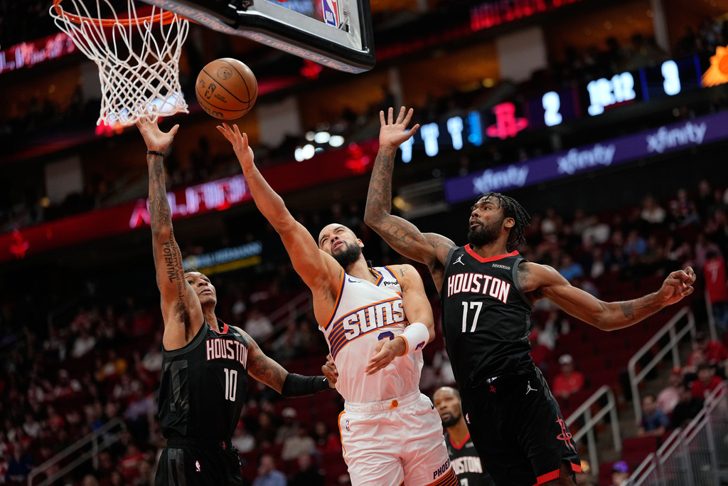 Phoenix Suns' Dillon Brooks, center, goes up for a shot as Houston Rockets' Jabari Smith Jr. (10) and Tari Eason (17) defend during the first half of an NBA basketball game Monday, Jan. 5, 2026, in Houston. (AP Photo/David J. Phillip)