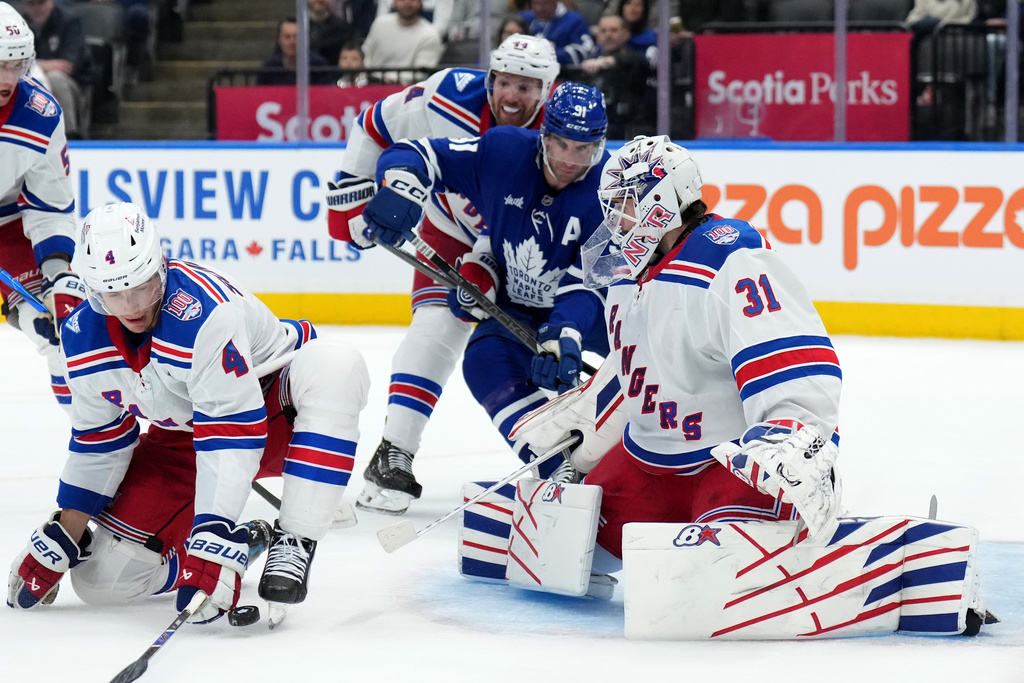 New York Rangers defenceman Braden Schneider (4) blocks a shot on teammate Igor Shesterkin (31) as Toronto Maple Leafs forward John Tavares (91) looks on during the second period of an NHL hockey game in Toronto, Wednesday, March 25, 2026. (Nathan Denette/The Canadian Press via AP)