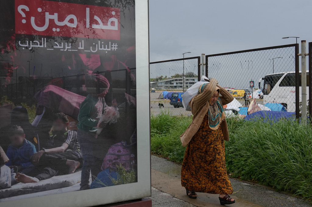 FILE — A displaced woman who fled Israeli airstrikes in southern Lebanon, carries her belonging as she moves to a better spot to shelter from the rain, past an Arabic anti-war poster that reads, "Sacrificing for whom? Lebanon does not need war," in Beirut, Saturday, March 21, 2026. (AP Photo/Hussein Malla, File)