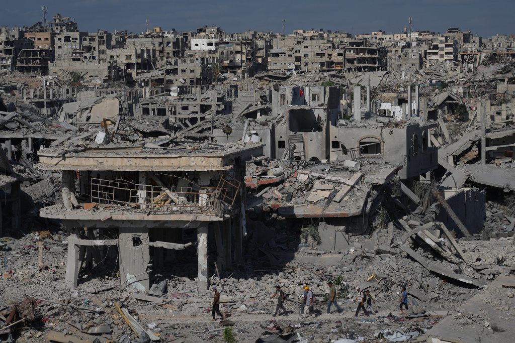 Displaced Palestinians walk through an area surrounded by destroyed buildings in Khan Younis, in the southern Gaza Strip, Saturday, Oct. 11, 2025, after Israel and Hamas agreed to a pause in their war and the release of the remaining hostages. (AP Photo/Jehad Alshrafi)