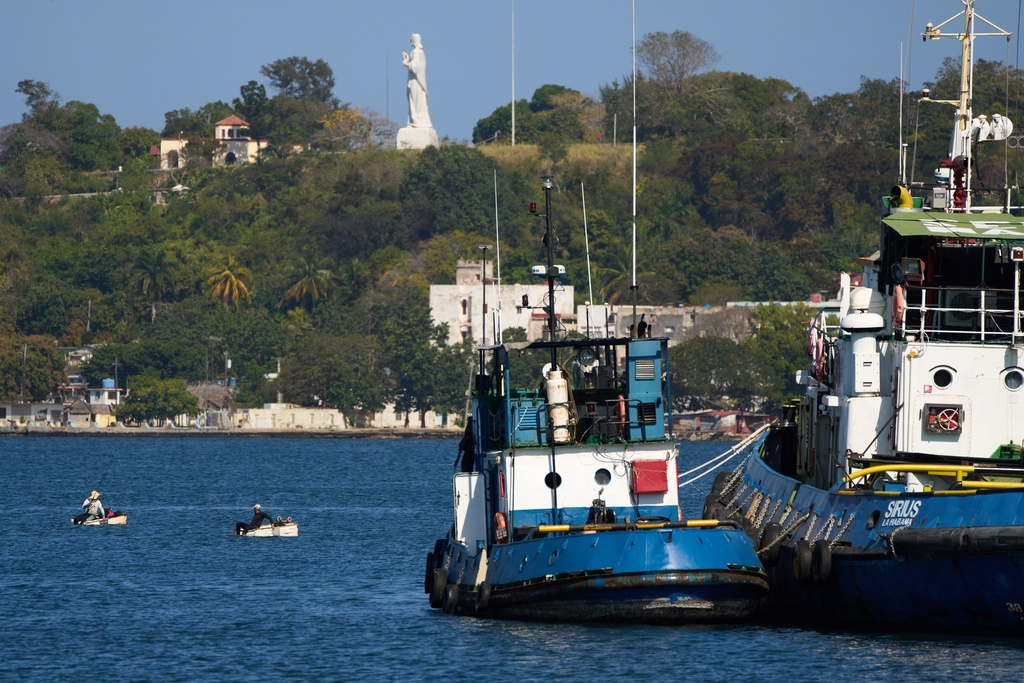 Two fisherman work from their makeshift "corcho" rafts, left, in Regla, Cuba, Thursday, Feb. 26, 2026. (AP Photo/Ramon Espinosa)