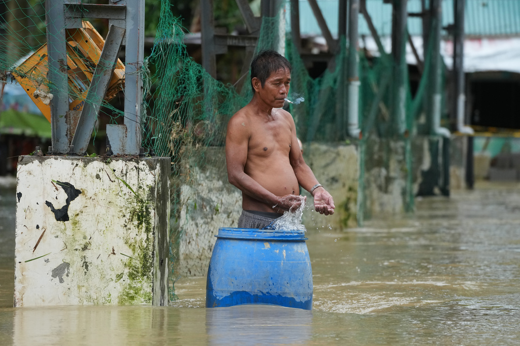 A man smokes along floodwaters caused by heavy seasonal monsoon rains at Bagong Silangan village in Quezon city, Metro Manila, Philippines, Monday, Aug. 10, 2026. (AP Photo/Aaron Favila)