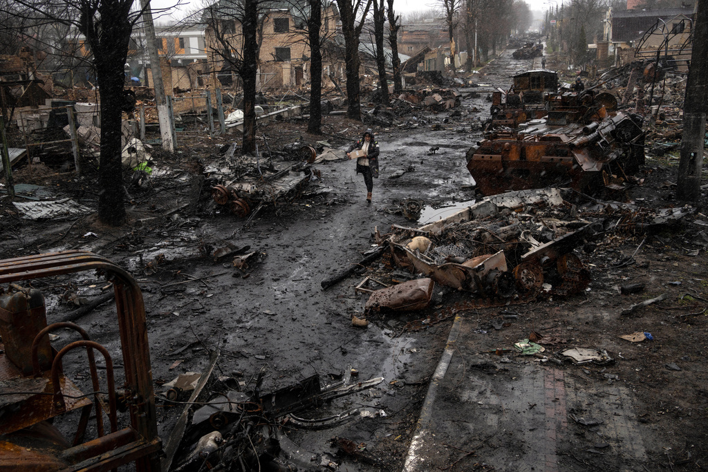 FILE - A woman navigates a debris-filled street where destroyed Russian military vehicles stand in Bucha on the outskirts of Kyiv, Ukraine, Sunday, April 3, 2022. (AP Photo/Rodrigo Abd, File)