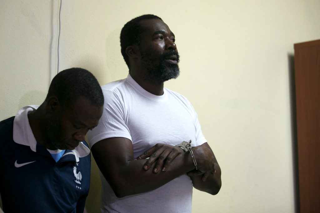 FILE - Former lawmaker Arnel Belizaire, right, stands in handcuffs as he is shown by the national police to the press along with other men, all arrested for carrying weapons and ammunition, in Port-au-Prince, Haiti, Dec. 4, 2019. (AP Photo/Dieu Nalio Chery, File)