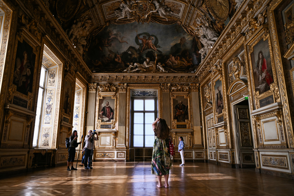 Visitors take a picture of the window which was broken during the reopening to the public of the Apollo Gallery, at the Louvre museum in Paris, Wednesday, July 22, 2026. (Lou Benoist/Pool Photo via AP)