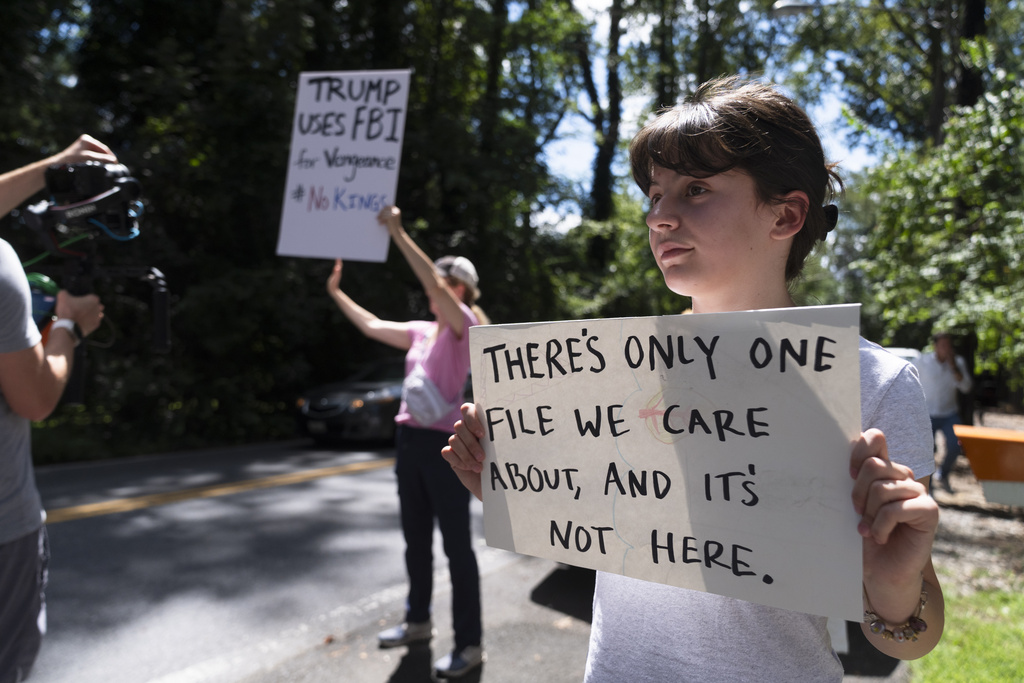 A young Bethesda resident holds a sign outside the house of former White House national security adviser John Bolton as FBI search the home, Friday, Aug. 22, 2025, in Bethesda, Md. (AP Photo/Manuel Balce Ceneta)