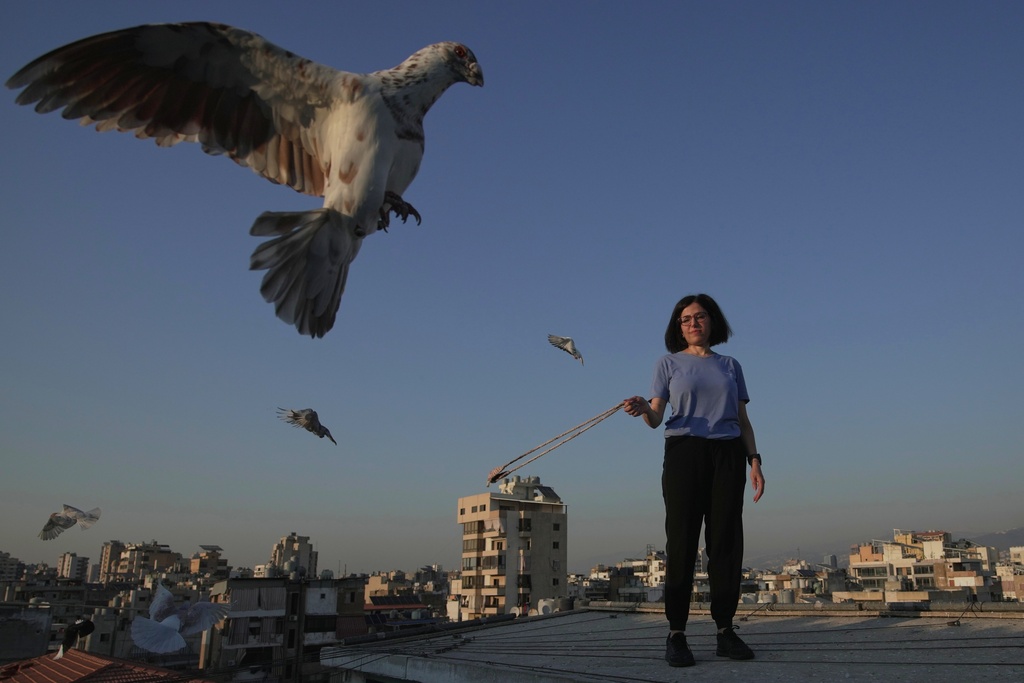 Loubna Hamdan stands on her loft's rooftop, where she leaves food out for pigeons, as she swings an empty slingshot to encourage them to fly and get exercise in Chiyah, the southern suburbs of Beirut, Lebanon, Lebanon, Thursday, July 10, 2025. (AP Photo/Hassan Ammar)