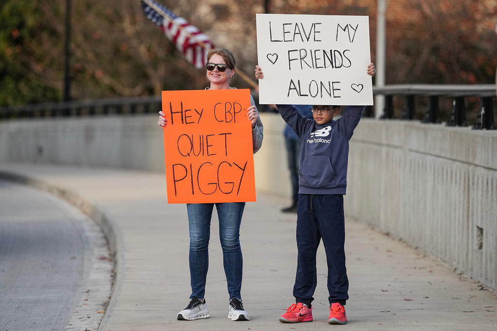 Protesters hold signs amid the arrival of federal law enforcement, Tuesday, Nov. 18, 2025, in Charlotte, N.C. (AP Photo/Matt Kelley)