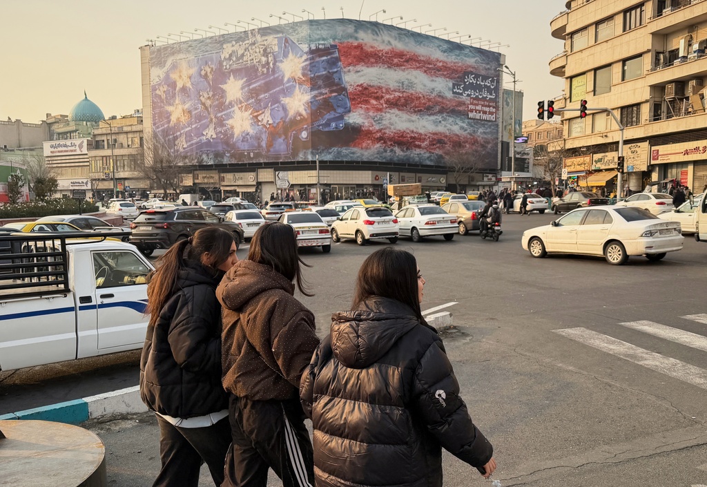 People walk in front a billboard with graphic showing a U.S aircraft carrier with damaged fighter jets on its deck, and sign reading in Farsi and English: "If you sow the wind, you'll reap whirlwind," at the Enqelab-e-Eslami (Islamic Revolution) square, in Tehran, Iran, Sunday, Jan. 25, 2026. (AP Photo/Vahid Salemi)