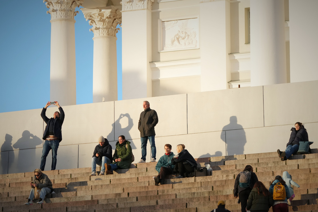 People enjoy the sunny weather with the Helsinki Cathedral of the background in Helsinki, Finland, Friday, Nov. 14, 2025. (AP Photo/Sergei Grits)