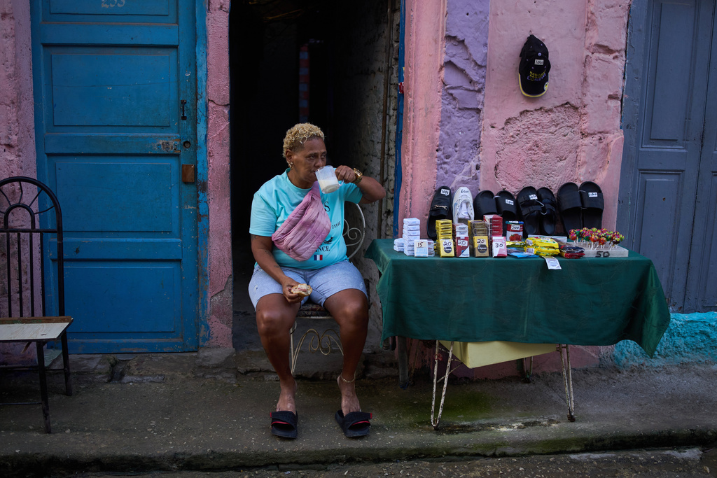 A vendor having breakfast sits by her table holding various products, from cigarettes to sandals, in Havana, Cuba, early Friday, March 13, 2026. (AP Photo/Ramon Espinosa)