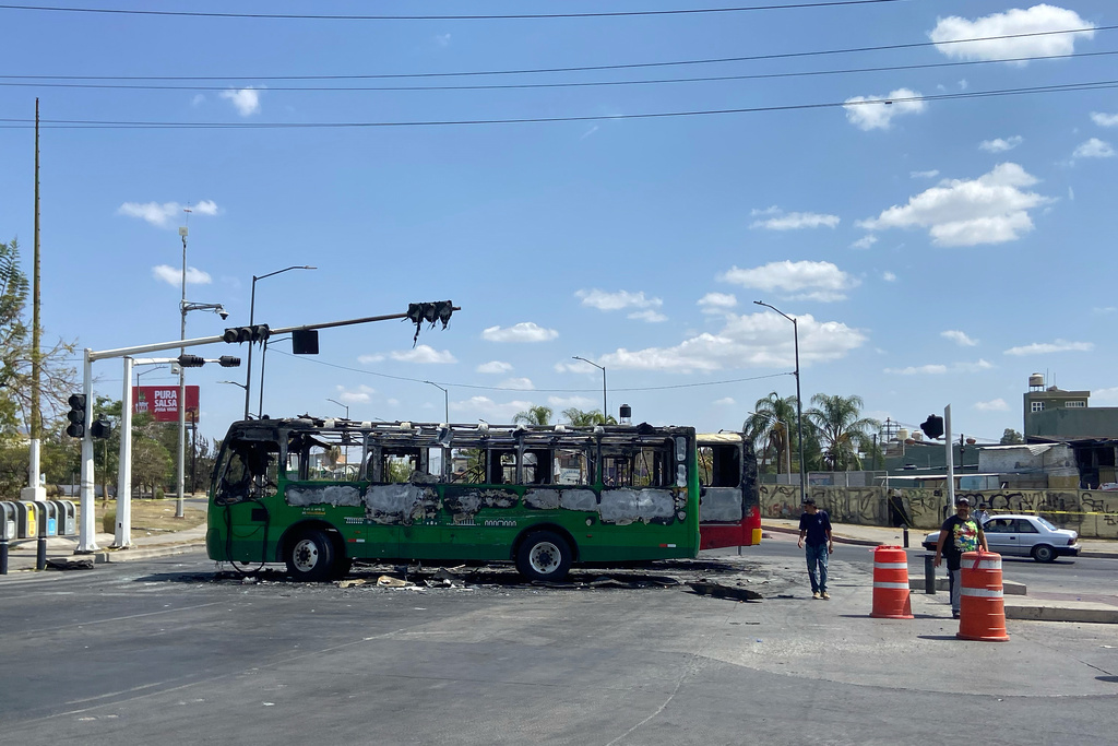 Pedestrians walk past charred buses that were set on fire, on a road in Guadalajara, Jalisco state, Mexico, Sunday, Feb. 22, 2026, after the death of the leader of the Jalisco New Generation Cartel, Nemesio Oseguera Cervantes, known as "El Mencho." (AP Photo/Refugio Ruiz)
