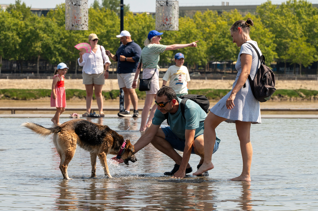 People with a dog cool off at the Miroir d'Eau reflecting pool outside the Place de la Bourse on a hot day in Bordeaux, France, Thursday, Aug. 13, 2026, as a heatwave affects much of the country. (AP Photo/Caroline Blumberg)
