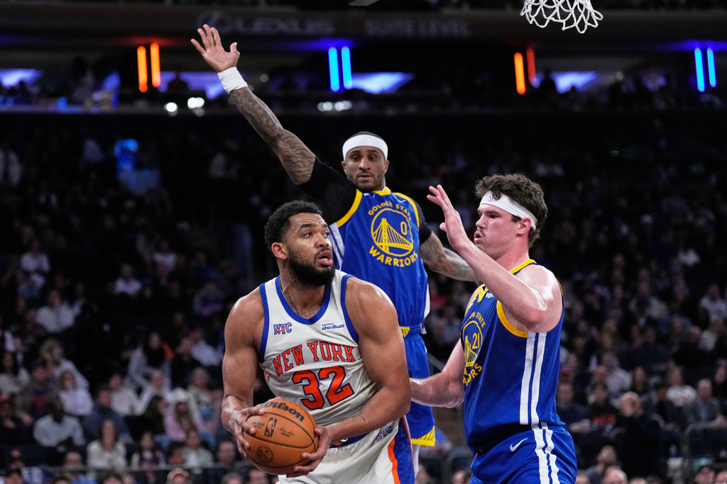 New York Knicks' Karl-Anthony Towns, left, looks to pass around Golden State Warriors defenders during the second half of an NBA basketball game Sunday, March 15, 2026, in New York. (AP Photo/Seth Wenig)