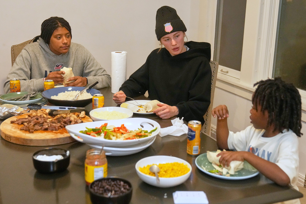 Laila Edwards, left, the first Black woman to suit up for Team USA women's Olympic hockey, teammate Caroline Harvey, center, and Laila's nephew Shiloh Stewart, right, talk during a family dinner at her childhood home in Cleveland Heights, Ohio, Wednesday, Nov. 5, 2025. (AP Photo/Sue Ogrocki)