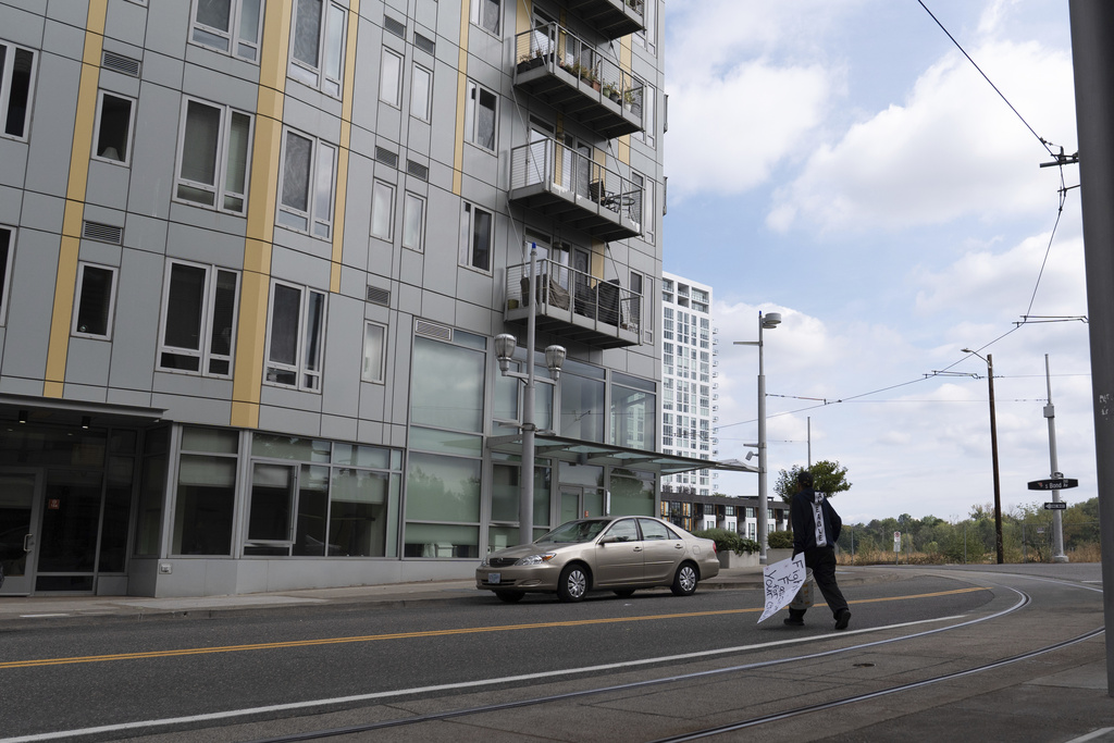 A worker walks to pick up litter while carrying a sign left outside the U.S. Immigration and Customs Enforcement building close by in Portland, Ore., on Tuesday, Sept. 9, 2025. (AP Photo/Jenny Kane)