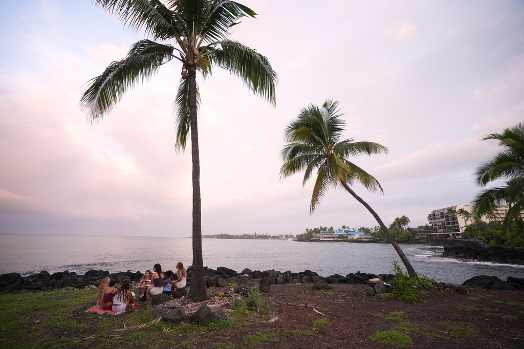 Members of Youth With A Mission read under a palm tree as Hurricane Nolo sits nearby Friday, Sept. 25, 2026, in Kona, Hawaii. (AP Photo/Gregory Bull)