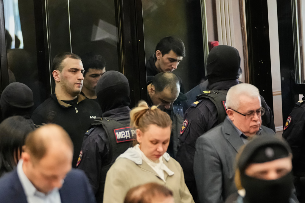 Men tried on the charges of involvement in a terror attack at the Crocus City Hall in March 2024, background, listen to the verdict from behind a glass cage at the Second Western District Military Court in Moscow, Russia, Thursday, March 12, 2026. (AP Photo/Pavel Bednyakov)
