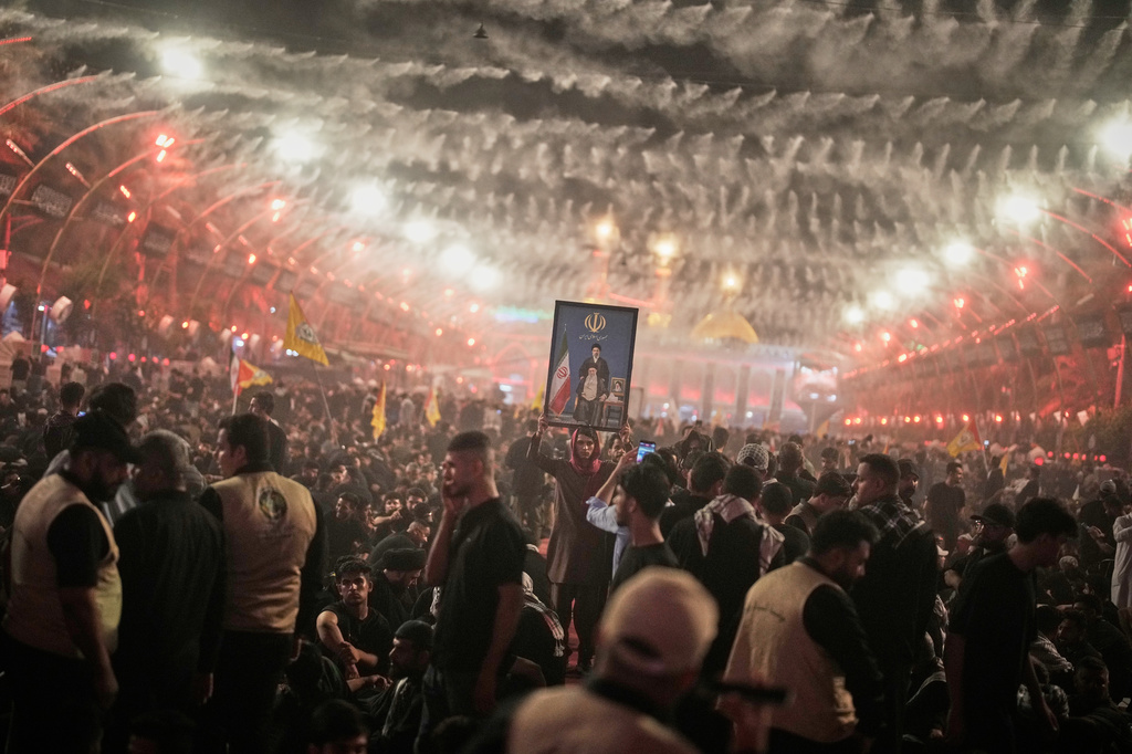 A mourner holds a portrait depicting Iran's Supreme Leader Ayatollah Mojtaba Khamenei, top, and his late father, Ayatollah Ali Khamenei, as mourners wait for the funeral procession for the elder Khamenei outside the Imam Hussein Shrine in Karbala, Iraq, Wednesday, July 8, 2026. (AP Photo/Khalil Hamra)