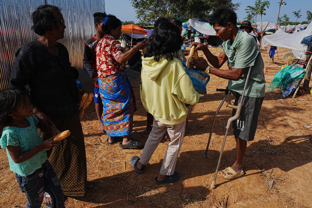A disabled man, right, receives bread from a local charity group as he takes refuge in Wat Prasat Srahkandal, Banteay Menchey province, Cambodia, Sunday, Dec. 14, 2025, after fleeing home following fighting between Thailand and Cambodia over territorial claims. (AP Photo/Heng Sinith)
