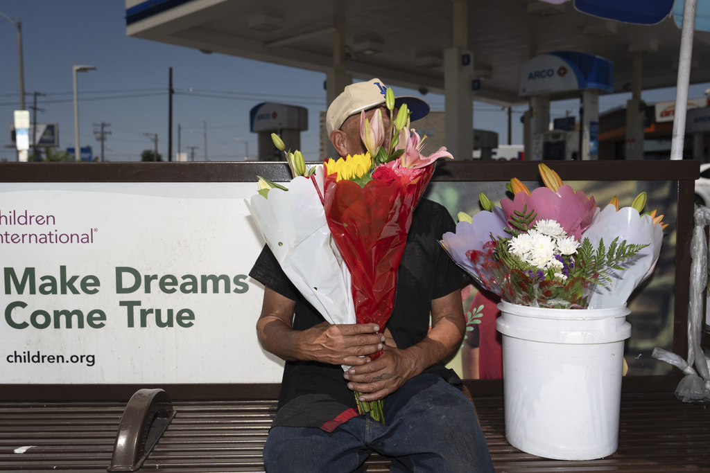 Flower vendor Jose, an immigrant from Mexico, sits for a photo with his face covered by flowers outside a gas station in Los Angeles, Friday, Aug. 8, 2025. (AP Photo/Jae C. Hong)