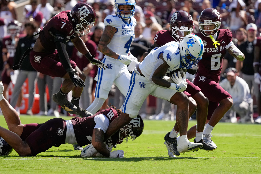 Kentucky's CJ Baxter Jr. (1) rushes for a first down as Texas A&M defensive end T.J. Searcy (18) and cornerback Dezz Ricks (2) defend during the first half of an NCAA college football game Saturday, Sept. 19, 2026, in College Station, Texas. (AP Photo/David J. Phillip)