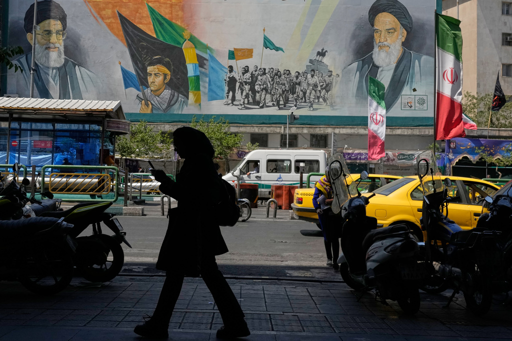 A woman walks on a sidewalk in front of a mural showing portraits of the late Iranian revolutionary founder Ayatollah Khomeini, right, the slain Supreme Leader Ayatollah Ali Khamenei, who was killed in U.S. and Israeli strikes on Feb. 28, and Basij paramilitary forces, at the Islamic Revolution street in Tehran, Iran, Monday, June 8, 2026. (AP Photo/Vahid Salemi)