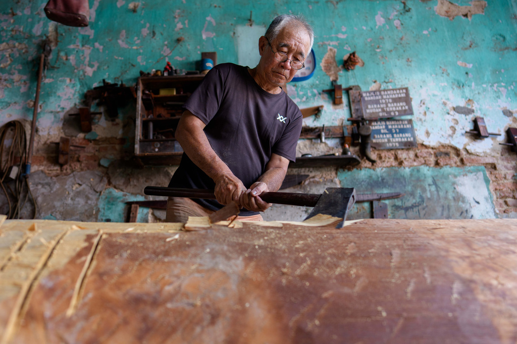 Goh Khuay Hou uses an axe to shape a wooden section during the early stages of making a Mei Hua coffin at his family's workshop in Muar, Malaysia, Monday, Sept. 7, 2026. (AP Photo/Vincent Thian)