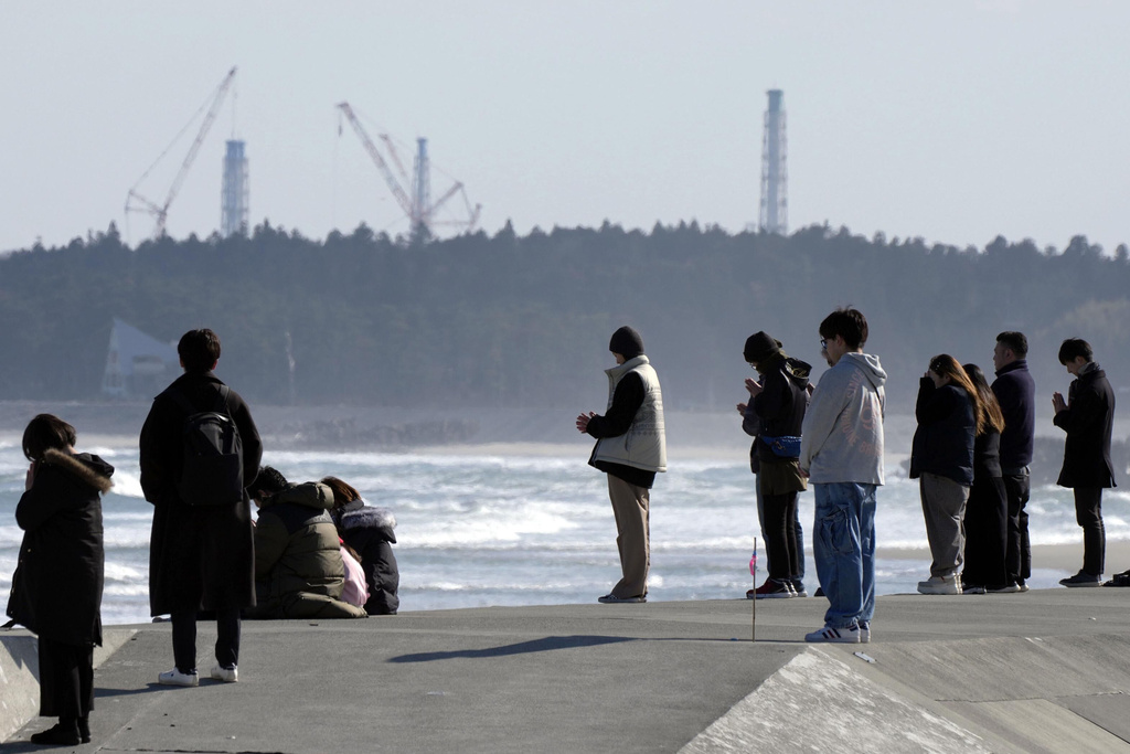 People observe a moment of silence at 2:46 p.m., the moment the earthquake struck with a backdrop of Fukushima Daiichi nuclear power plant in Namie, Fukushima prefecture, northern Japan as the country marked the 15th anniversary of the massive earthquake, tsunami and nuclear disaster. (Kyodo News via AP)