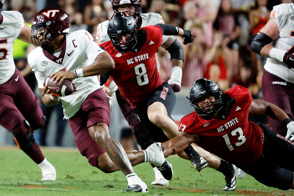 Virginia Tech quarterback Kyron Drones (1) avoids the rush of North Carolina State defensive end Travali Price (13), and Isaiah Crowell (8) during the first half of an NCAA college football game in Raleigh, N.C., Saturday, Sept. 27, 2025. (AP Photo/Karl DeBlaker)