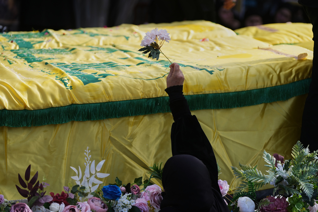 A woman places flowers on coffins of Hezbollah fighters who were killed before the ceasefire in the war between Hezbollah and Israel, during a mass funeral procession in the southern village of Kfar Sir, Lebanon, Tuesday, April 21, 2026. (AP Photo/Hassan Ammar)